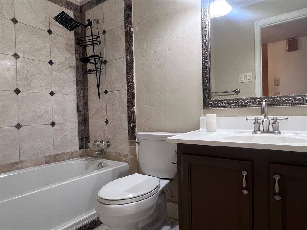 3925 Villa Downs Drive, Plano, TX 75023 Bathtub with tiled surround, rain shower head, toilet, vanity with integrated sink, and framed mirror