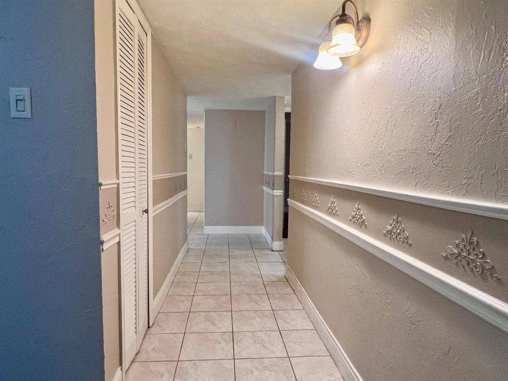 3925 Villa Downs Drive, Plano, TX 75023 Hallway featuring tile flooring, textured walls, chair rail molding with decorative appliques, and a built-in storage closet with louvered bifold doors