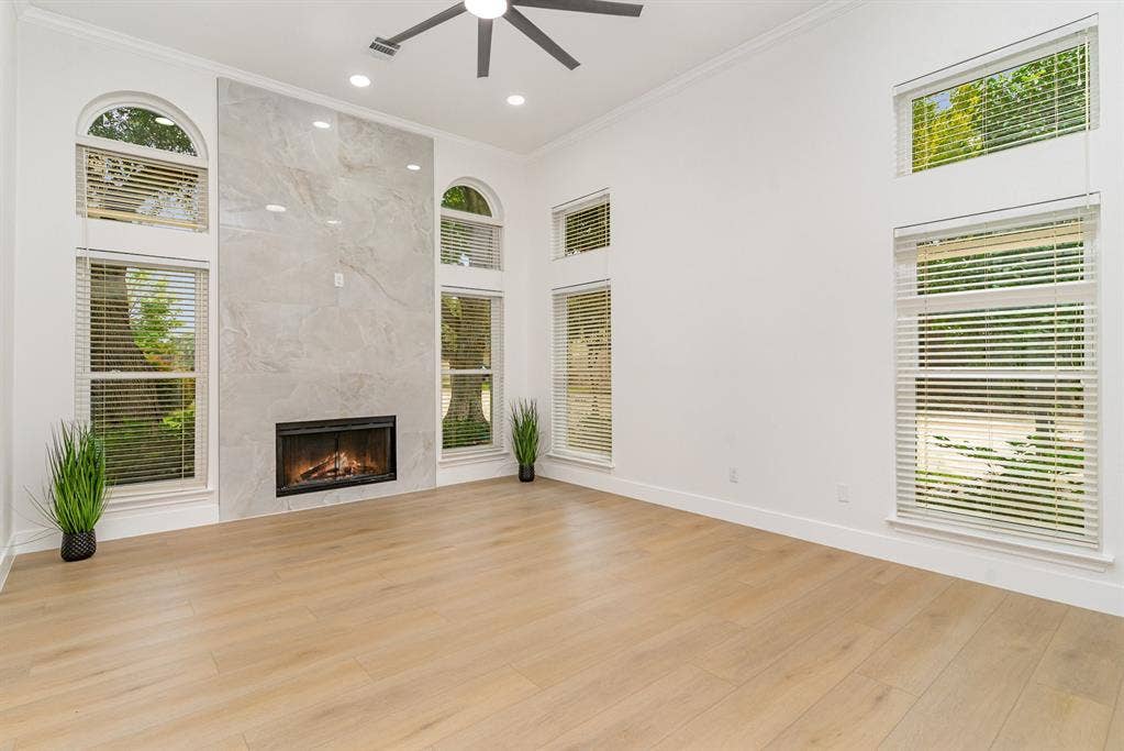 17732 Windflower Way, Dallas, TX 75252 Unfurnished living room with ornamental molding, ceiling fan, a premium fireplace, a towering ceiling, and light wood-type flooring