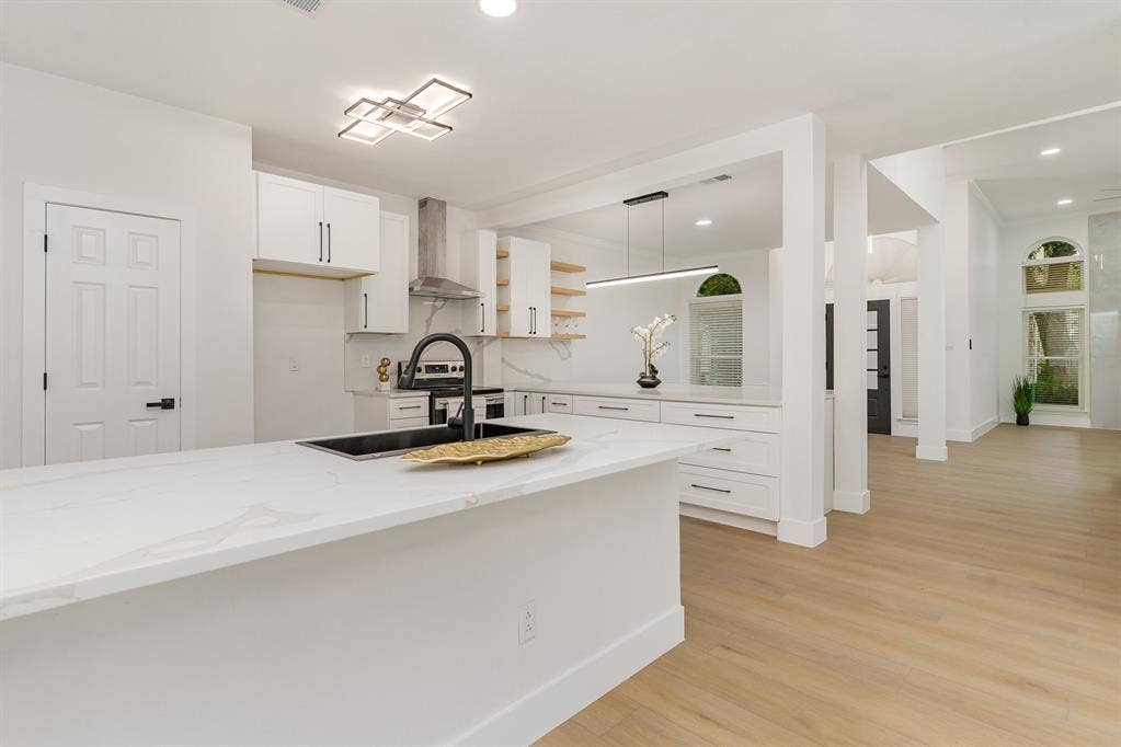 17732 Windflower Way, Dallas, TX 75252 Kitchen featuring hanging light fixtures, wall chimney range hood, light stone countertops, white cabinetry, and light hardwood / wood-style flooring