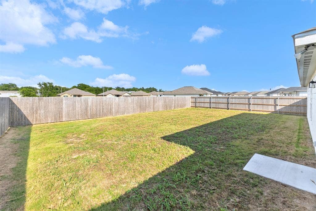 Expansive backyard featuring a wood privacy fence, concrete patio, and mature landscaping