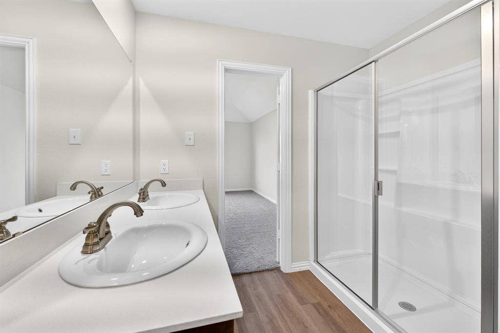 Dual vanity with white countertops, wood-finish flooring, and a glass-enclosed shower