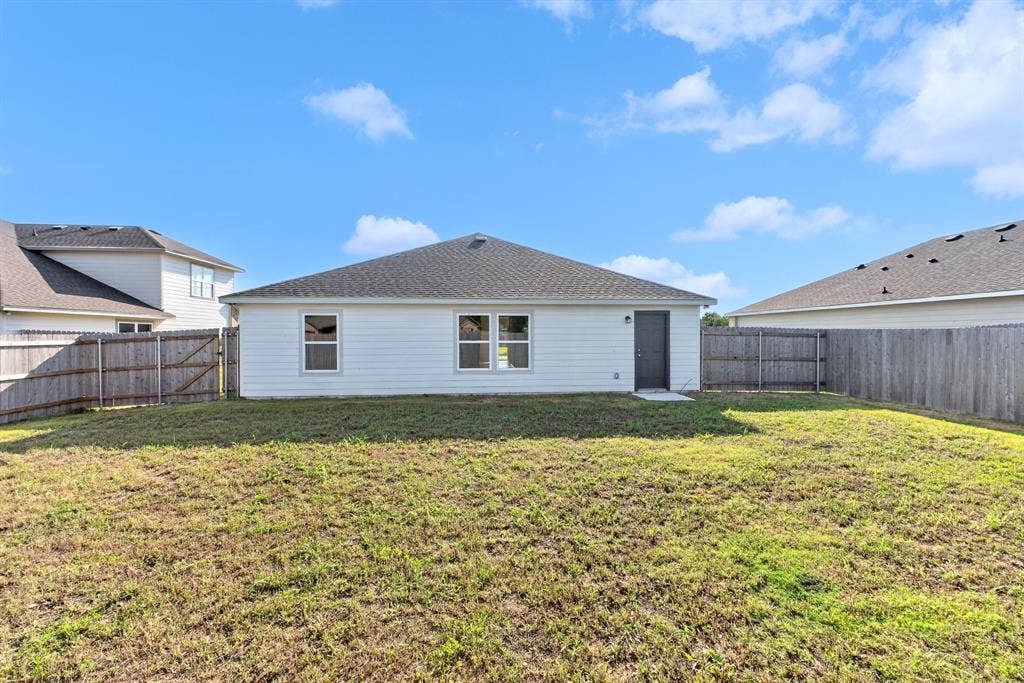 Expansive fenced backyard featuring a wood fence, white siding exterior, multiple windows, and a side entry door