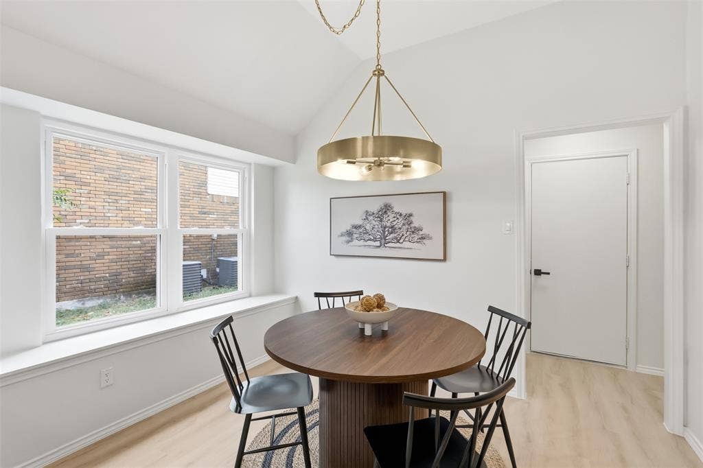 Vaulted ceiling, contemporary chandelier, light wood-finish flooring, white walls, and a large window with a deep sill
