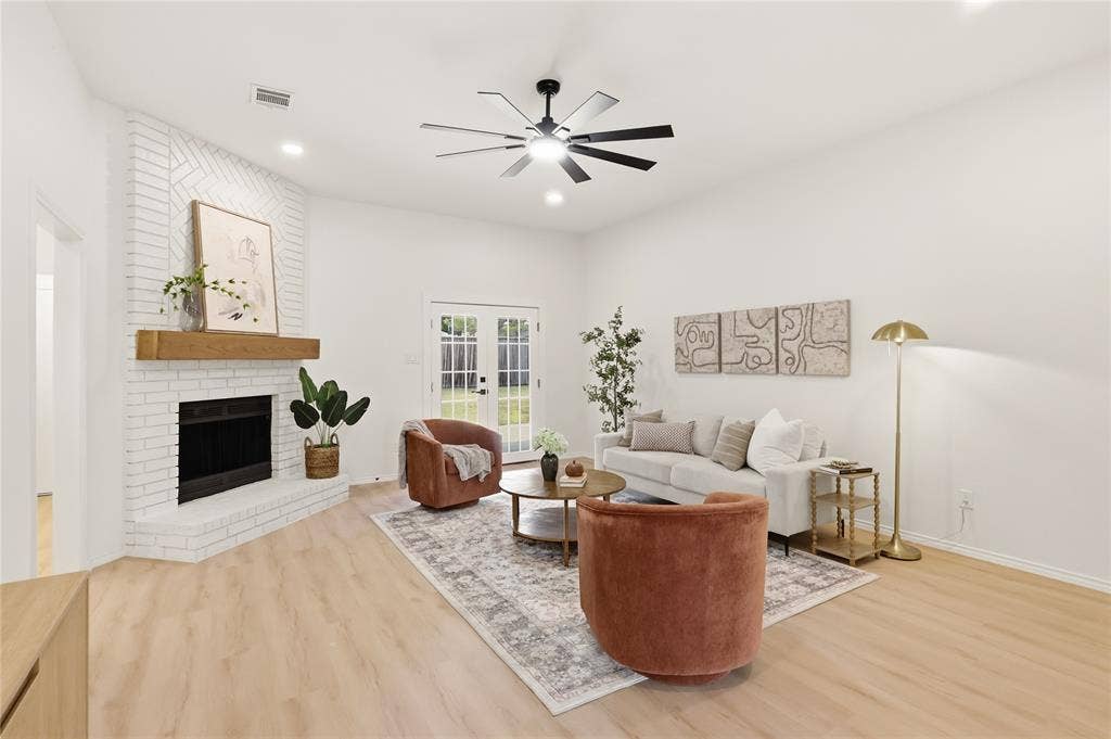 Bright living area with a white brick fireplace, wood mantel, and light wood-finish flooring
