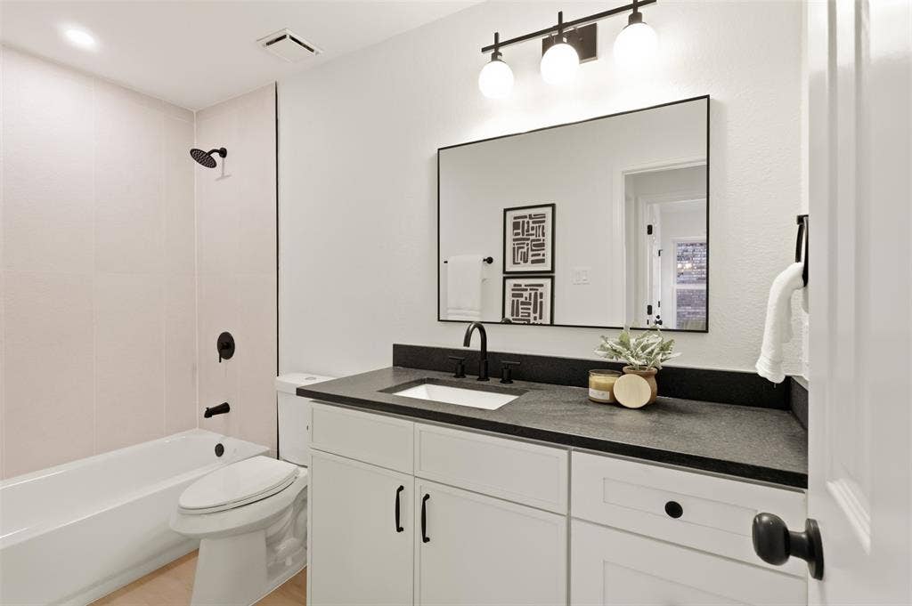 Bathroom featuring white cabinetry, a dark countertop, an undermount sink with a matte black faucet, and a large framed mirror