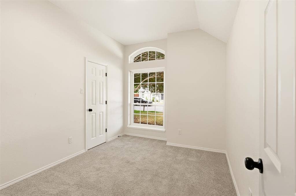 Room featuring vaulted ceiling, arched transom window, paneled doors, and gray carpeting