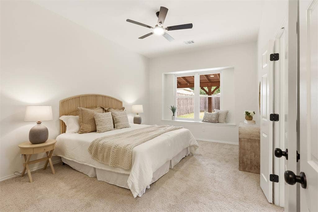 Recessed window alcove, ceiling fan, white paneled door, black door hardware, and light-toned carpet