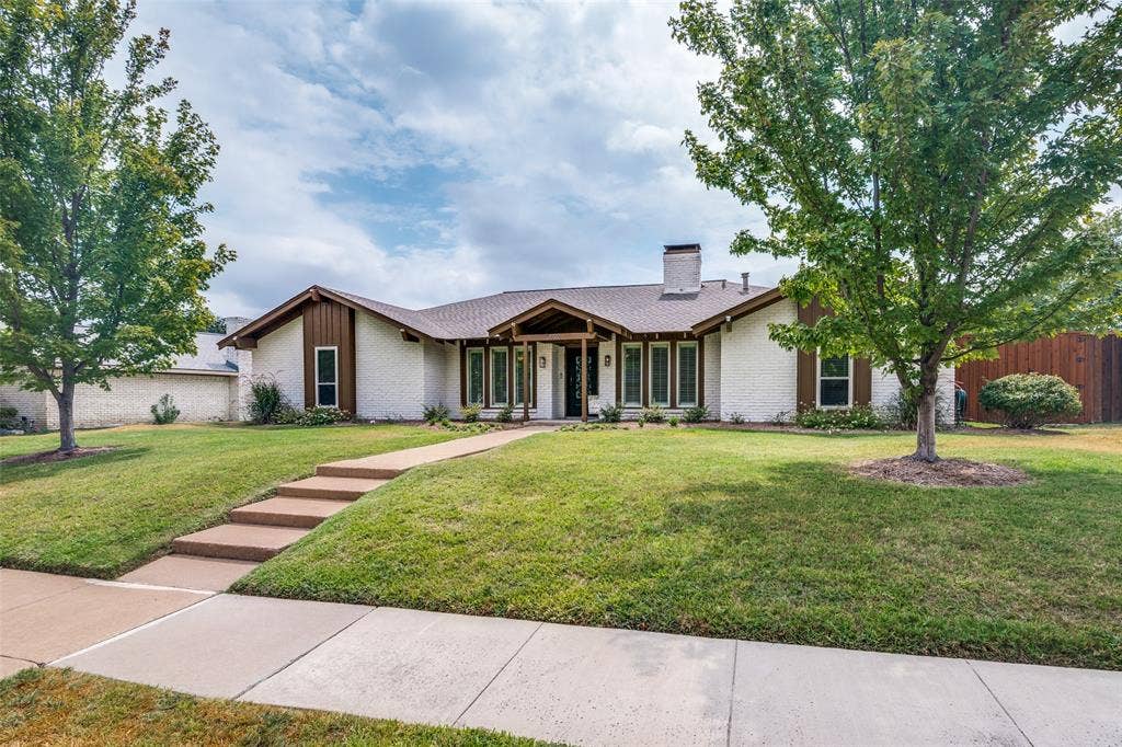 3632 Candelaria Drive, Plano, TX 75023 Contemporary ranch-style residence featuring a stucco exterior with wood-trimmed architectural accents, positioned on an expansive manicured lawn framed by mature shade trees