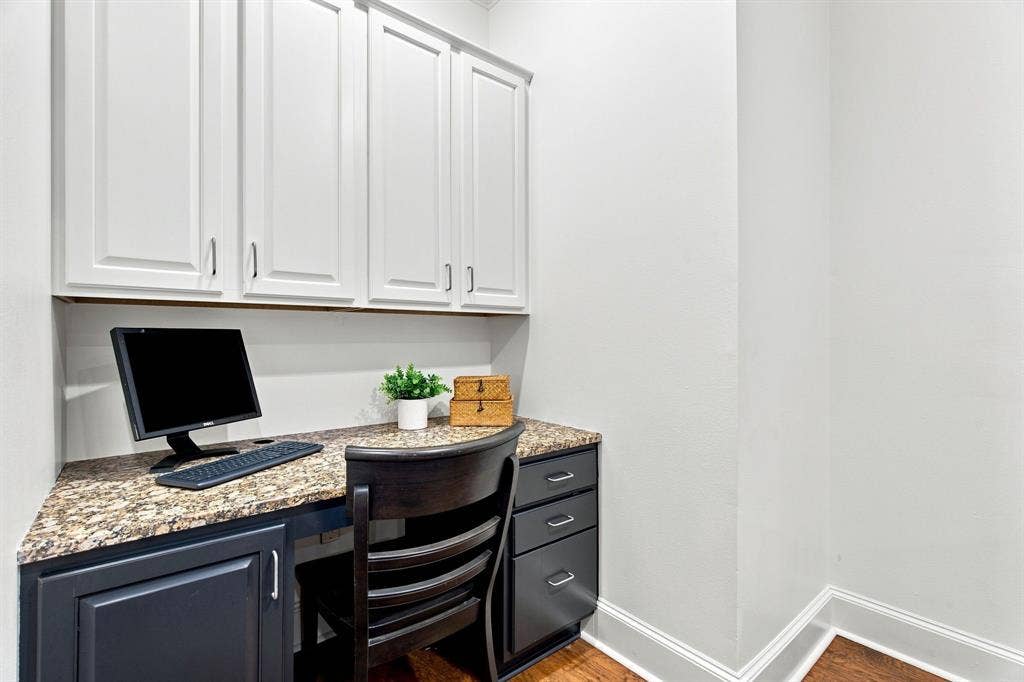 3303 Blackburn Street, #306, Dallas, TX 75204 Built-in desk with a stone-finish countertop, white upper cabinetry, dark lower cabinetry, and wood-finish flooring off of the breakfast nook.