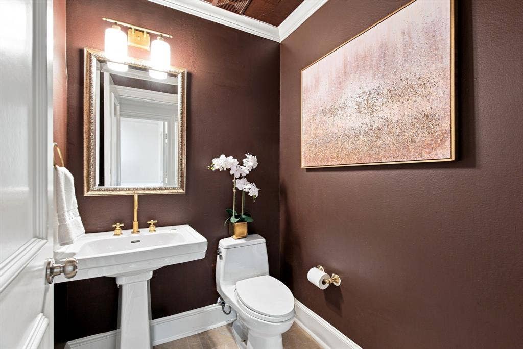3303 Blackburn Street, #306, Dallas, TX 75204 Half bathroom adjacent to living room with a eedestal sink with brass-finish faucet, framed mirror, and wall-mounted vanity light.