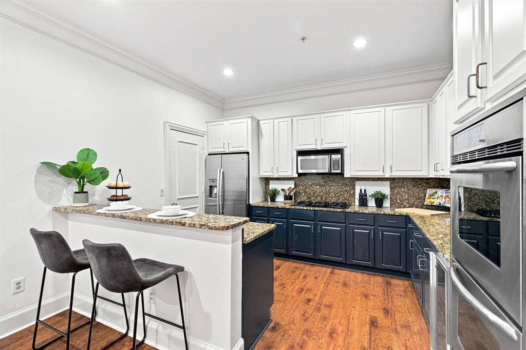 3303 Blackburn Street, #306, Dallas, TX 75204 Kitchen featuring wood-finish flooring, two-tone cabinetry, stainless steel appliances, granite countertops, and recessed lighting