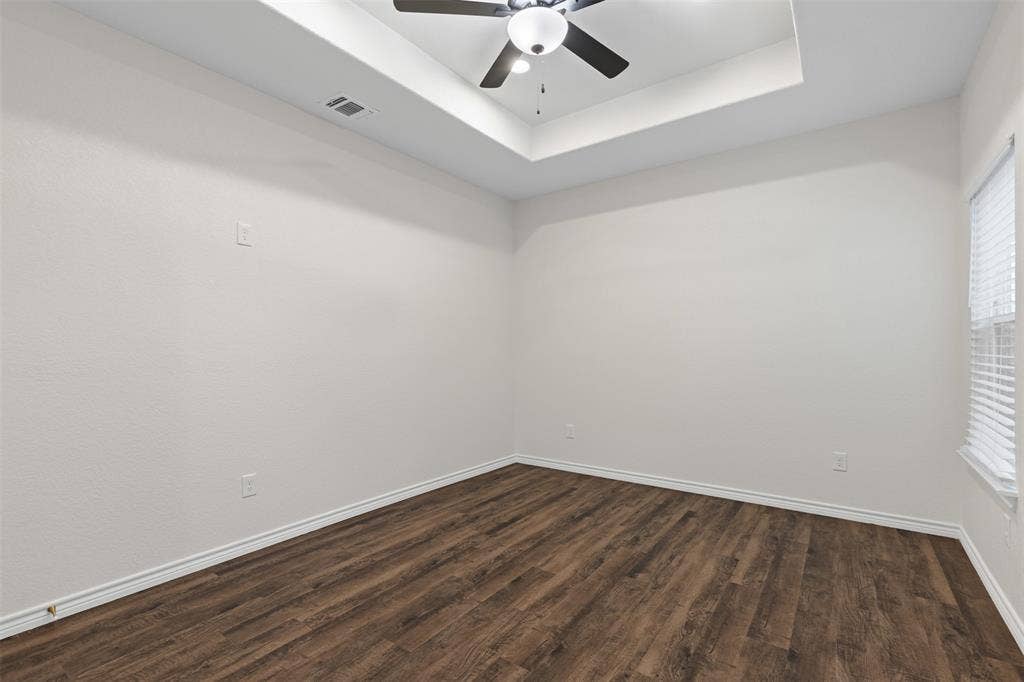 Empty room with dark wood-style flooring, a ceiling fan, a tray ceiling, and baseboards
