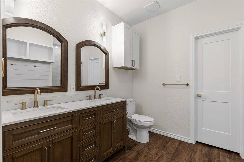 Bathroom featuring double vanity, toilet, wood finished floors, and baseboards