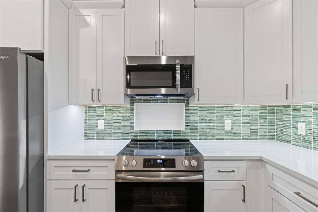 Kitchen featuring stainless steel appliances, white cabinetry, light countertops, and tasteful backsplash