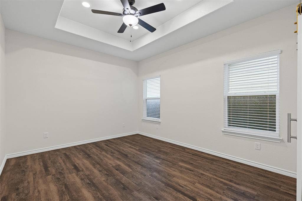 Empty room featuring a raised ceiling, dark wood-style floors, baseboards, and recessed lighting