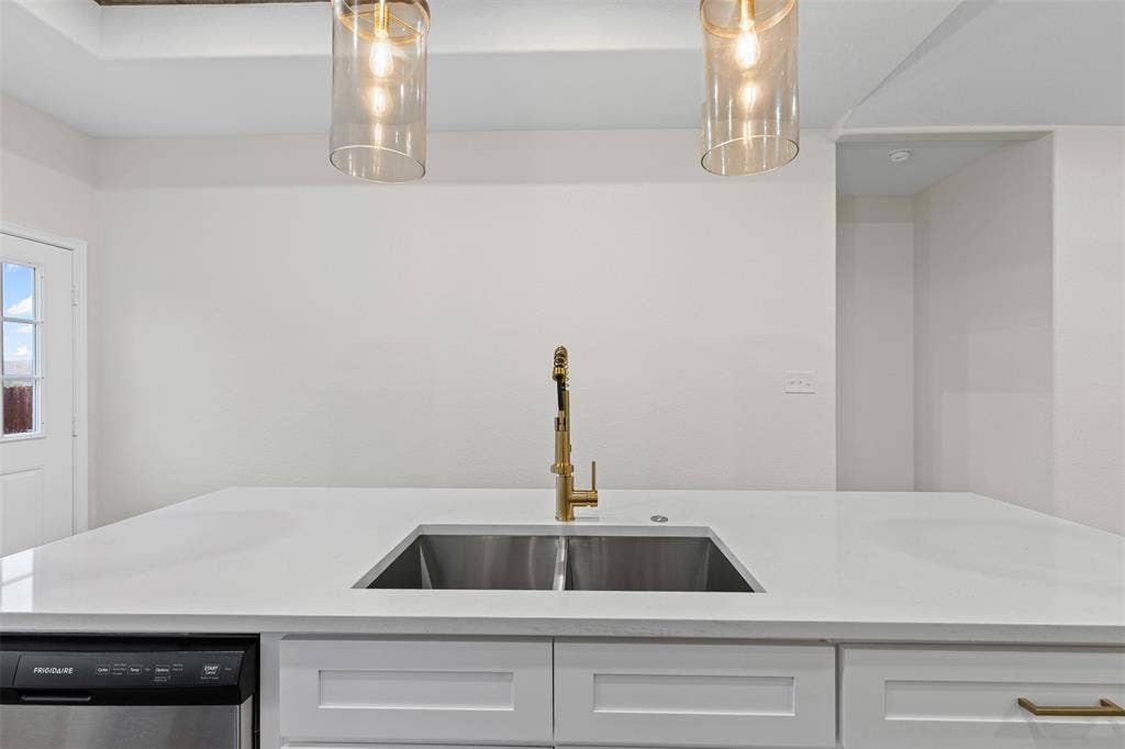 Kitchen with stainless steel dishwasher, a sink, white cabinetry, and light countertops