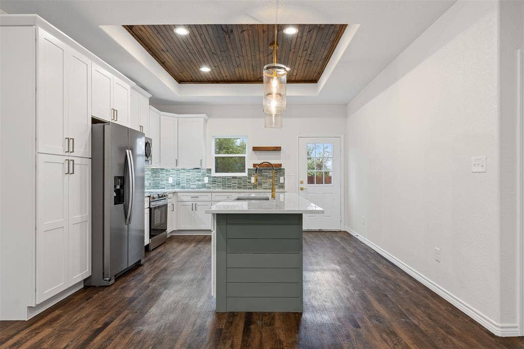 Kitchen featuring a tray ceiling, appliances with stainless steel finishes, a sink, light countertops, and dark wood-type flooring