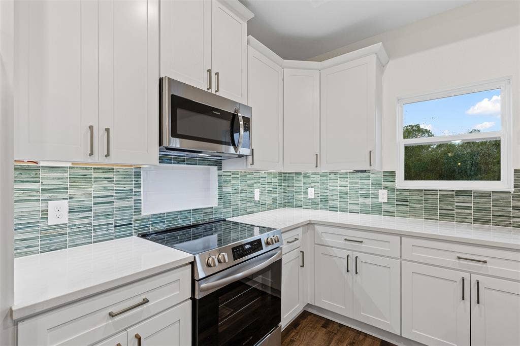 Kitchen featuring appliances with stainless steel finishes, white cabinetry, backsplash, and dark wood-style floors