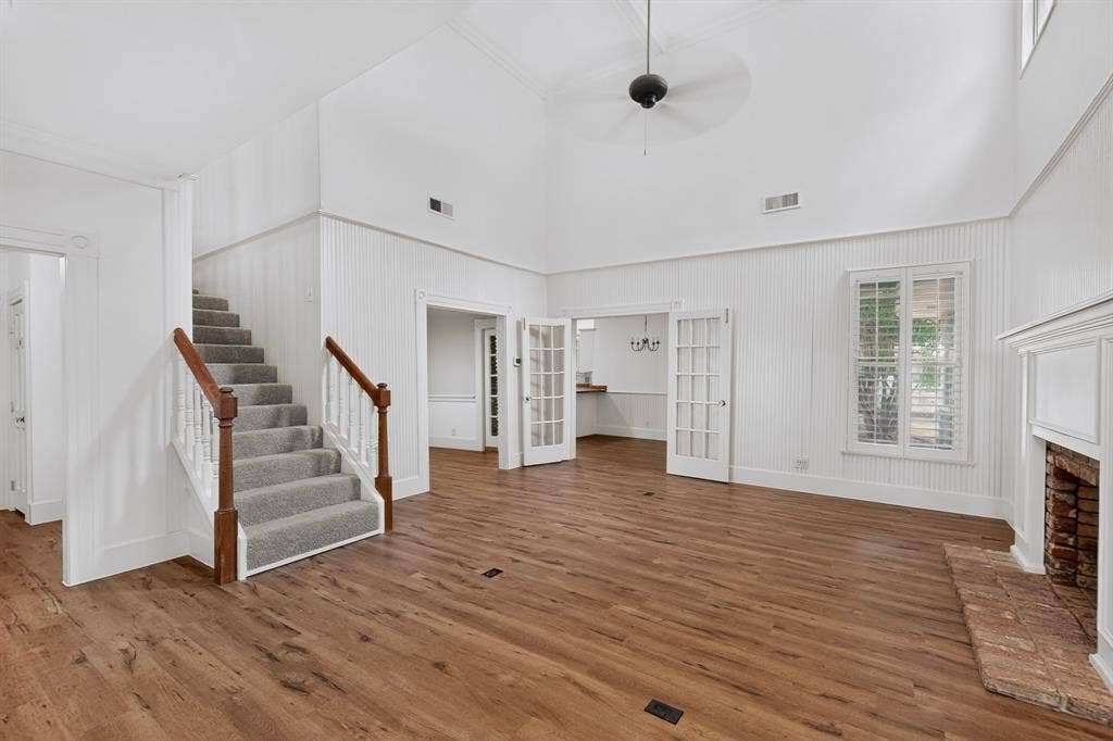 2 Trailridge Drive, Melissa, TX 75454 High vaulted ceiling with a ceiling fan, wood-finish flooring, white shiplap wall paneling, brick fireplace with a white mantel, and a carpeted staircase with wood handrails