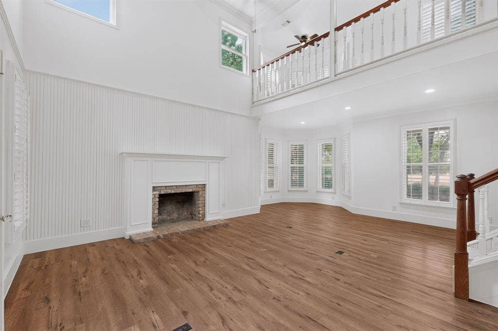 2 Trailridge Drive, Melissa, TX 75454 Two-story living area with wood-finish flooring, a brick fireplace with a white mantel, and a bay window featuring plantation shutters