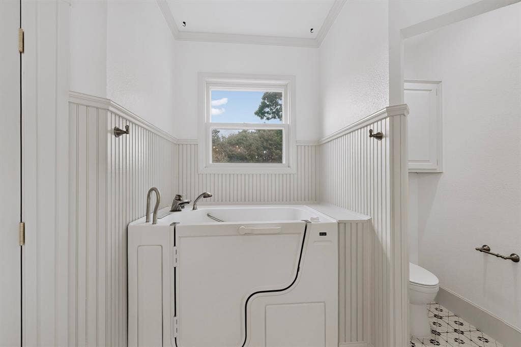 2 Trailridge Drive, Melissa, TX 75454 Walk-in bathtub with chrome fixtures, wainscoting, window with exterior scenery, and patterned tile flooring