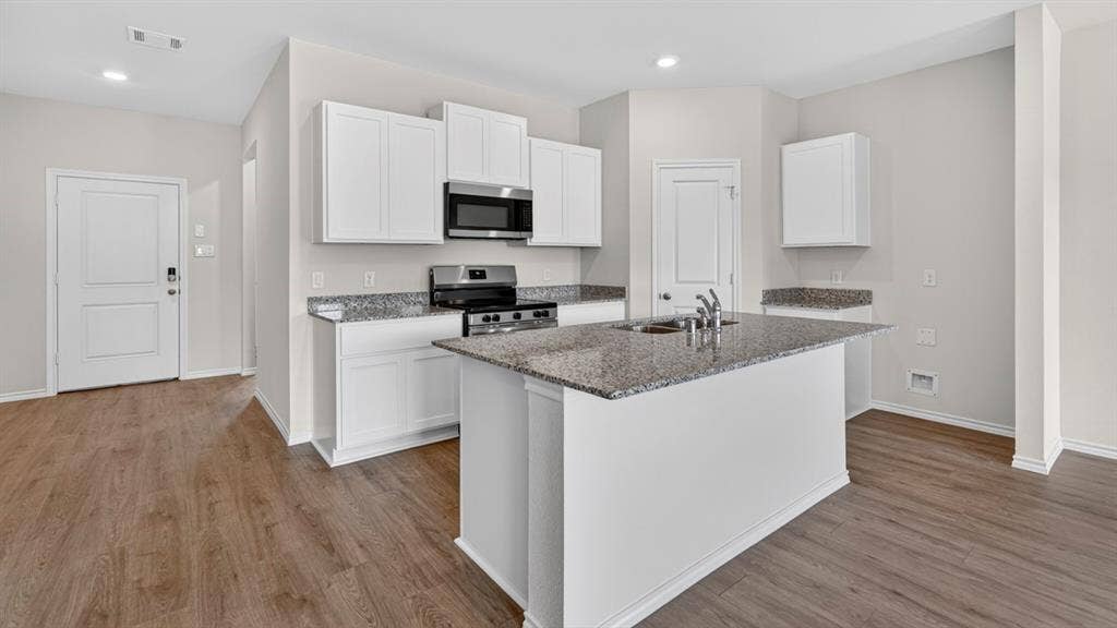1920 Freeman Street, Tyler, TX 75704 Kitchen featuring an island with a dual-basin sink, stainless steel appliances, granite countertops, white cabinetry, and wood-finish flooring