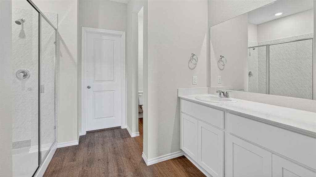 1920 Freeman Street, Tyler, TX 75704 Bathroom featuring a glass-enclosed shower, wood-finish flooring, white vanity with integrated sink, and an expansive wall mirror