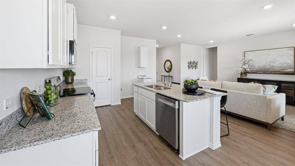 1932 Freeman Street, Tyler, TX 75704 Open-concept kitchen featuring white cabinetry, granite-finish countertops, stainless steel appliances, a central island with a double sink, and wood-finish flooring