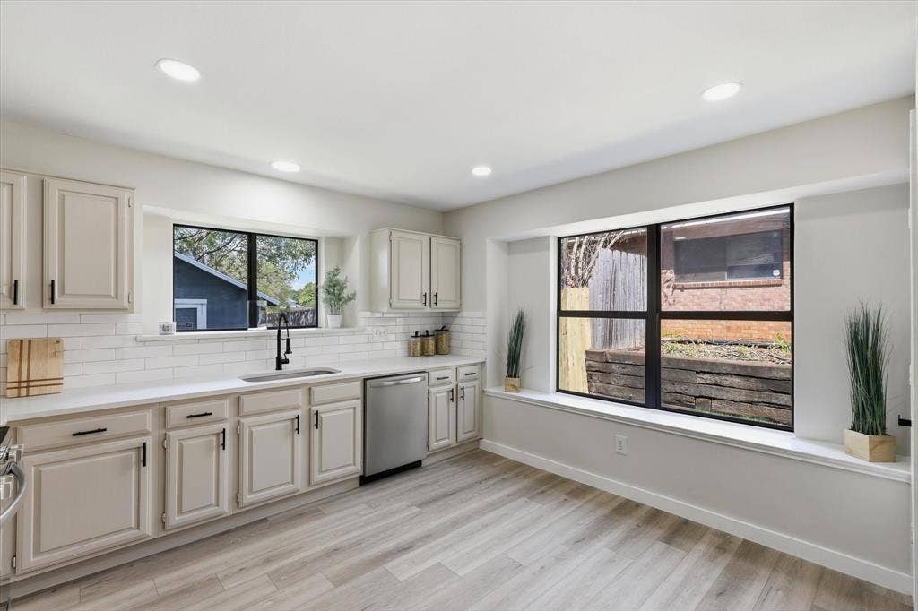 3405 Mill Ridge, Bedford, TX 76021 Recessed lighting illuminates the kitchen featuring light-toned cabinetry, a stainless steel dishwasher, white subway tile backsplash, and a large window above the sink