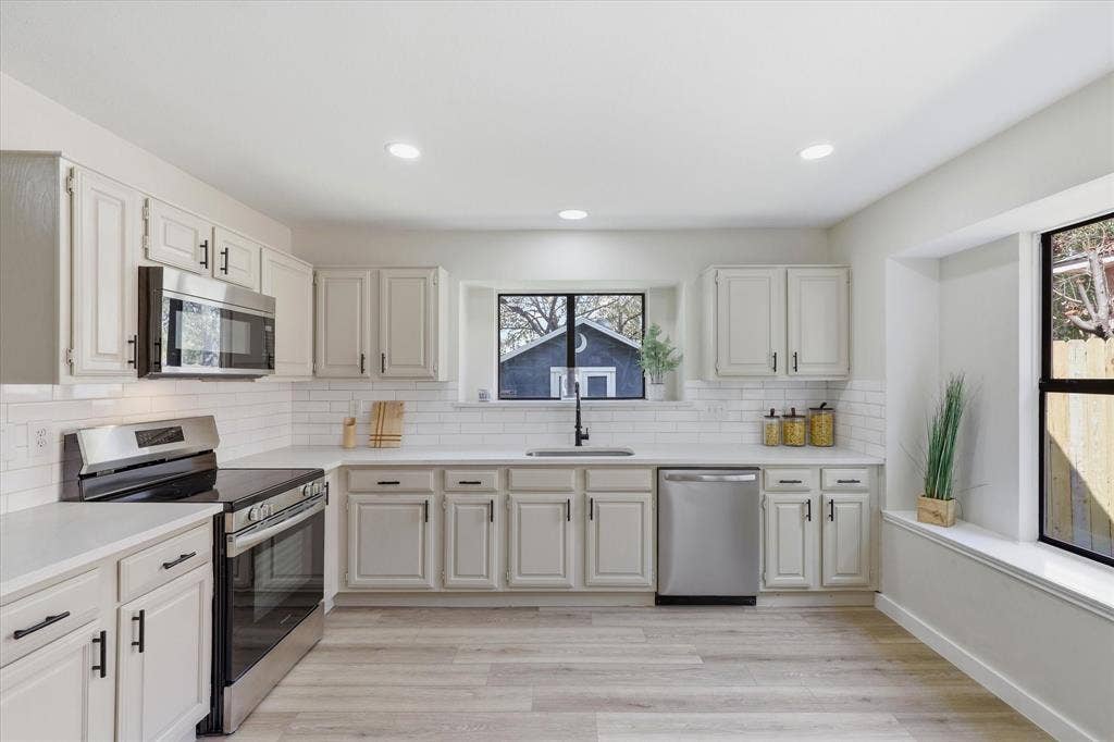 3405 Mill Ridge, Bedford, TX 76021 Contemporary kitchen featuring light wood-finish flooring, white cabinetry with black hardware, stainless steel appliances, and a white subway tile backsplash
