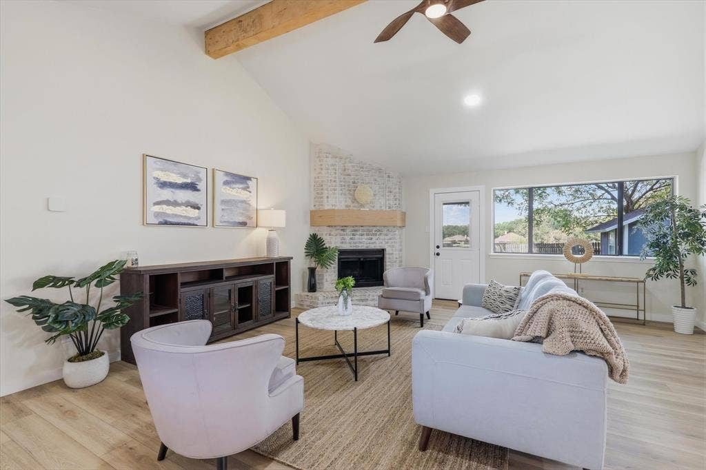 3405 Mill Ridge, Bedford, TX 76021 Vaulted ceiling with exposed wood beam, wood-finish flooring, white painted brick fireplace with wood mantel, large window, and ceiling fan