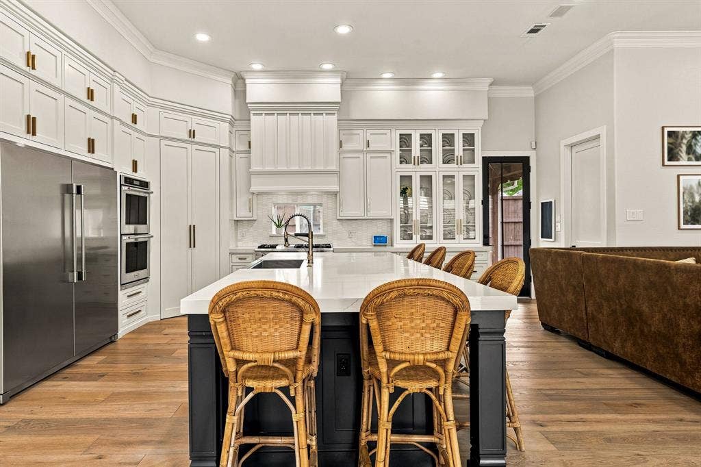 5941 Tiburon Drive, Plano, TX 75093 Spacious kitchen featuring an expansive island, stainless steel appliances, extensive white cabinetry, recessed lighting, and wood-finish flooring