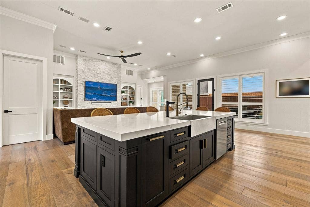 5941 Tiburon Drive, Plano, TX 75093 Open-concept living area featuring wood-finish flooring, a kitchen island with a white countertop and black cabinetry, a farmhouse sink, and recessed lighting