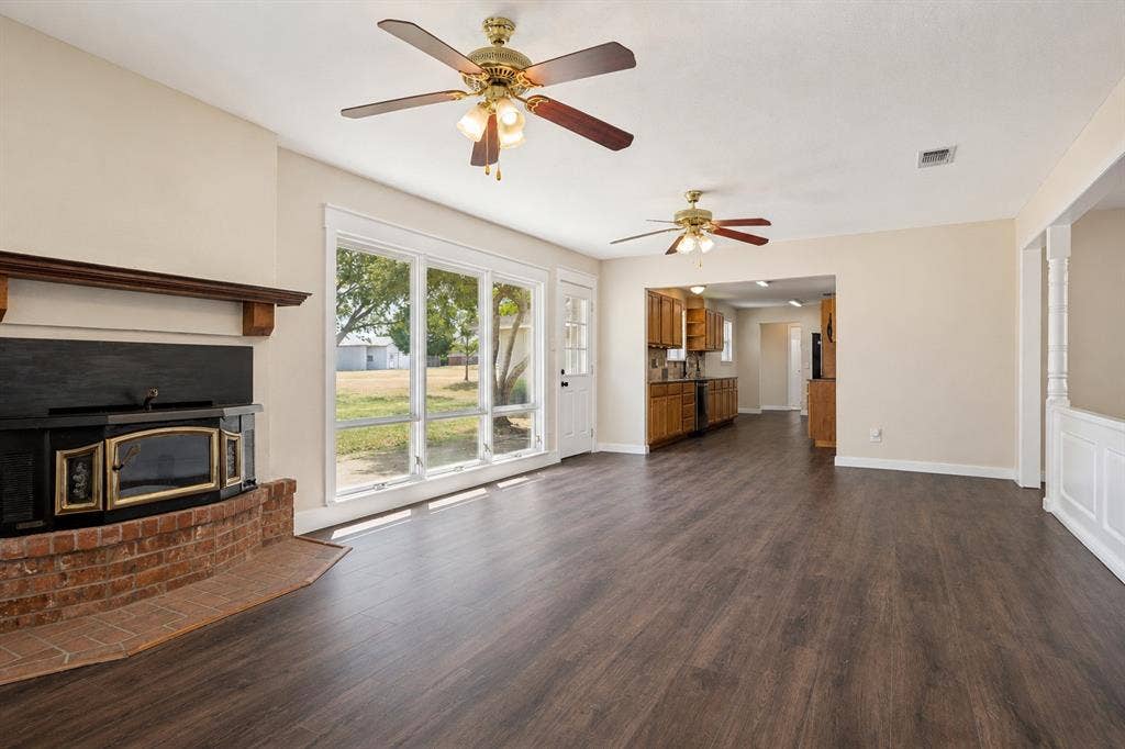2406 County Road 852, McKinney, TX 75071 Wood-finish flooring, brick-surround fireplace with wood mantel, multiple ceiling fans, and a multi-pane glass door leading to an exterior