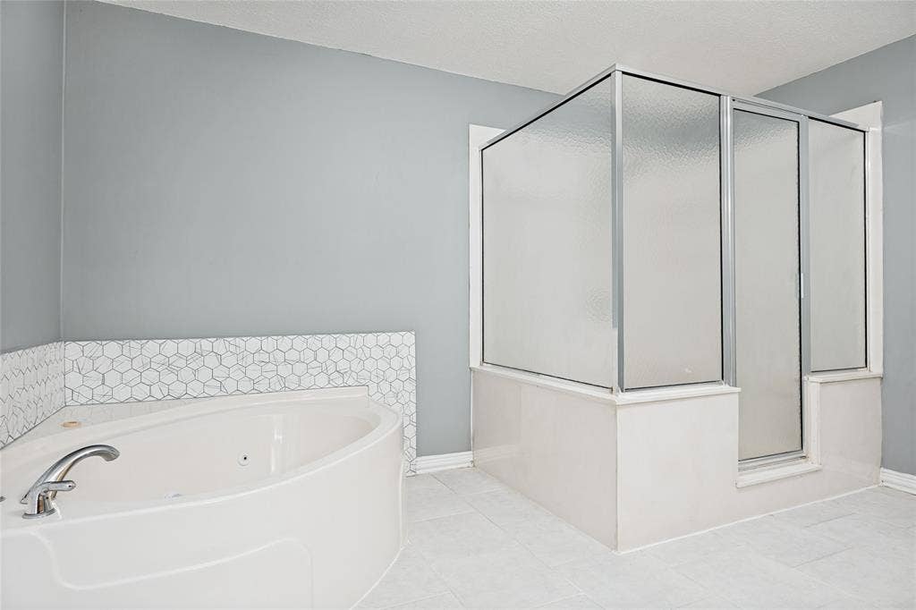 2406 County Road 852, McKinney, TX 75071 Corner tub, glass-enclosed shower, polished chrome fixtures, hexagonal tile accent, and light-toned floor tile