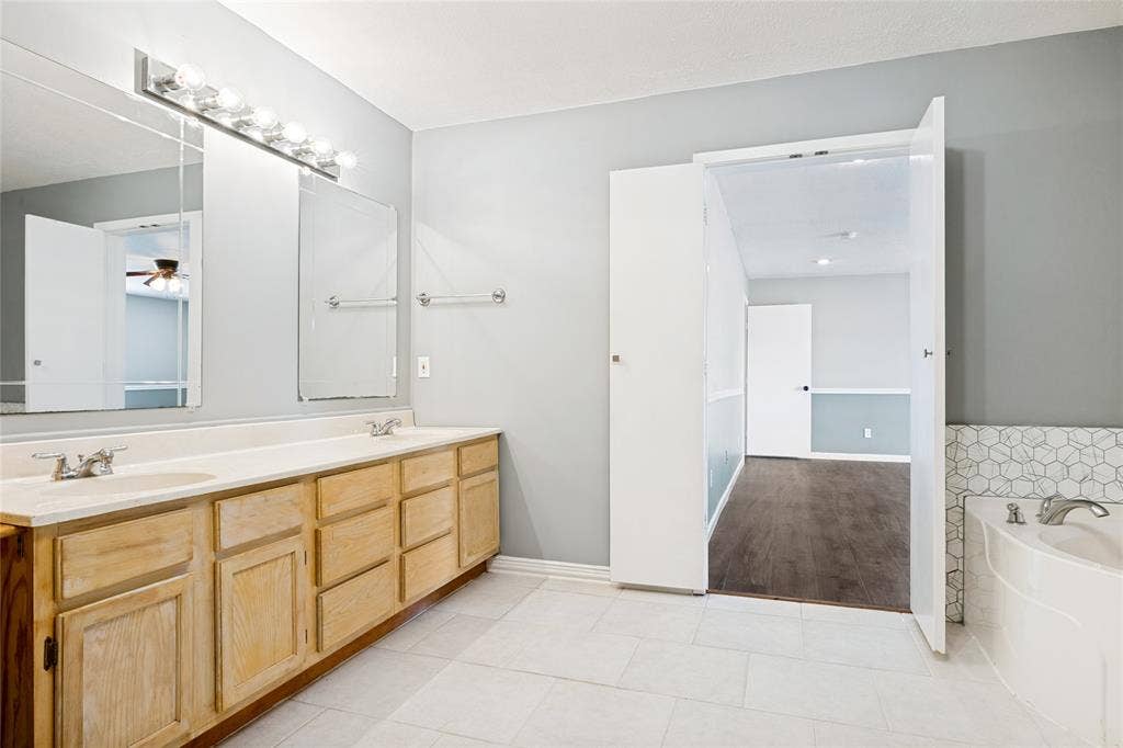 2406 County Road 852, McKinney, TX 75071 Double vanity with integrated sinks, large mirrors, overhead lighting fixture, hexagonal tile accent, and a built-in tub