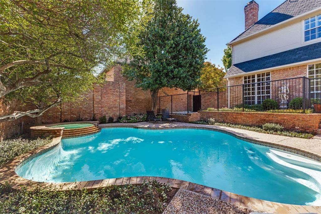 12012 Excelsior Way, Dallas, TX 75230 Freeform swimming pool with integrated spa and broad steps, surrounded by brick-edged coping and mature landscaping