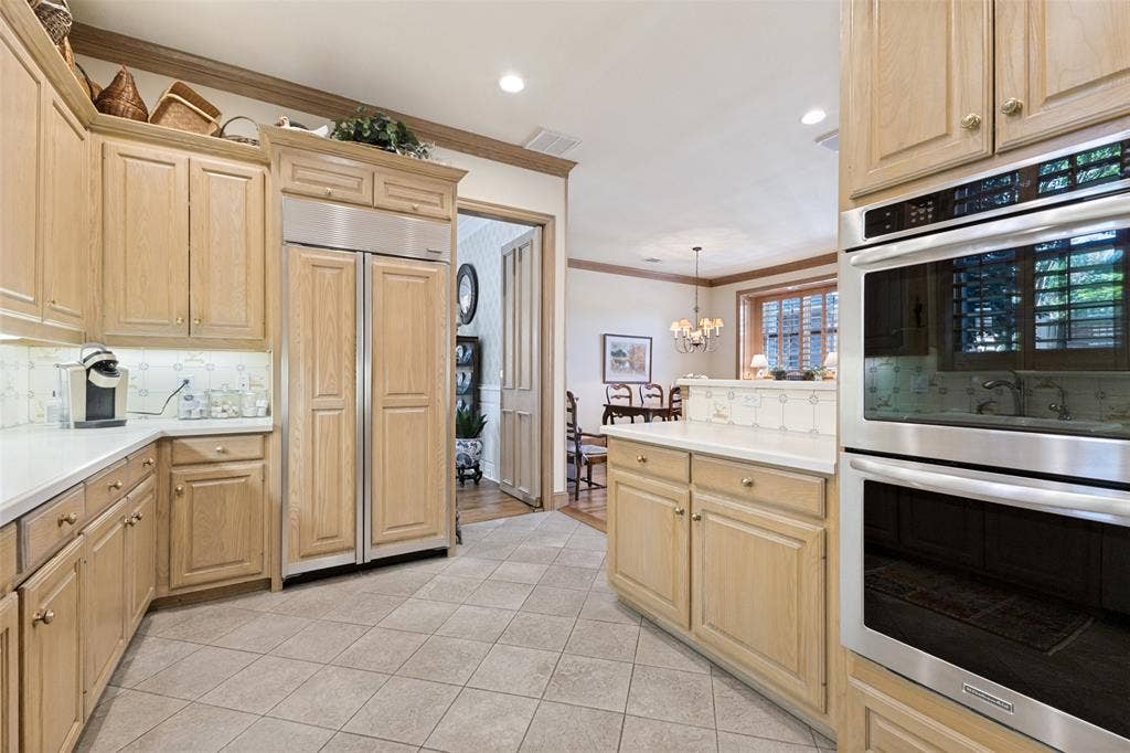 12012 Excelsior Way, Dallas, TX 75230 Light wood-finish cabinetry with gold-tone hardware, integrated stainless steel refrigerator, double wall ovens, white countertops, and tiled flooring