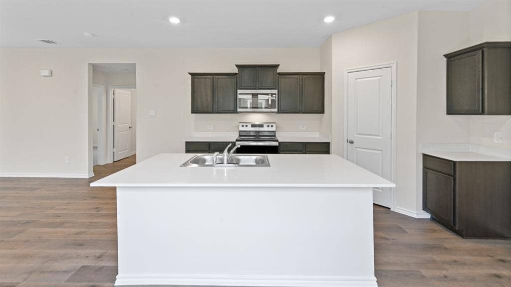 5806 Blue Sky Drive, Crandall, TX 75114 Modern kitchen island with an undermount sink, white countertops, dark wood-finish cabinetry, stainless steel appliances, and wood-finish flooring