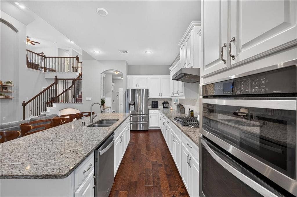 8712 Mccutchins Drive, McKinney, TX 75070 Spacious kitchen featuring white cabinetry, stainless steel appliances, granite countertops, an island with an undermount sink, and wood-finish flooring