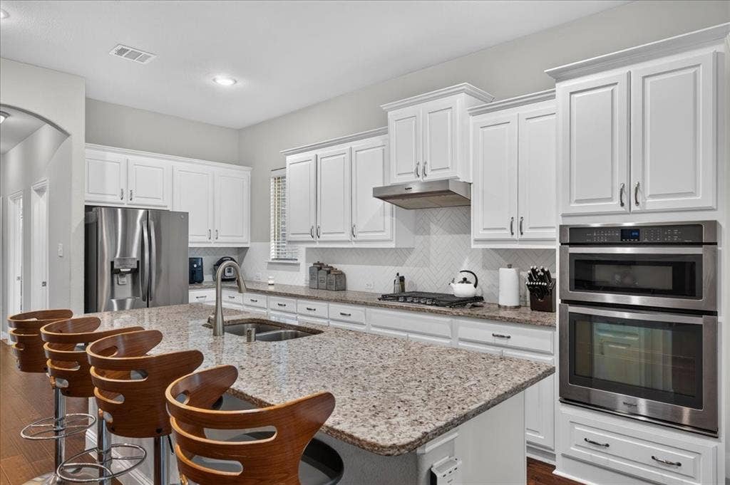 8712 Mccutchins Drive, McKinney, TX 75070 White shaker cabinetry with crown molding, granite countertops, stainless steel appliances, a built-in oven with microwave, and wood-finish flooring