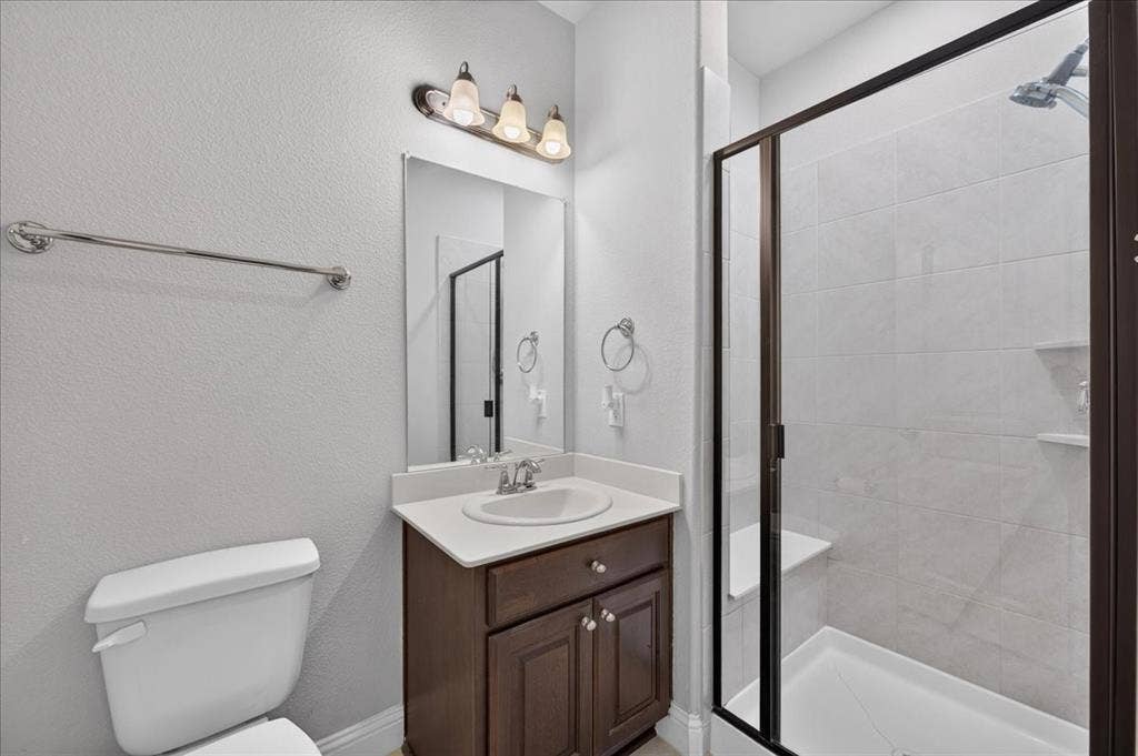 8712 Mccutchins Drive, McKinney, TX 75070 Bathroom featuring a dark wood-finish vanity, white countertop with an undermount sink, and a glass-enclosed shower with a built-in bench