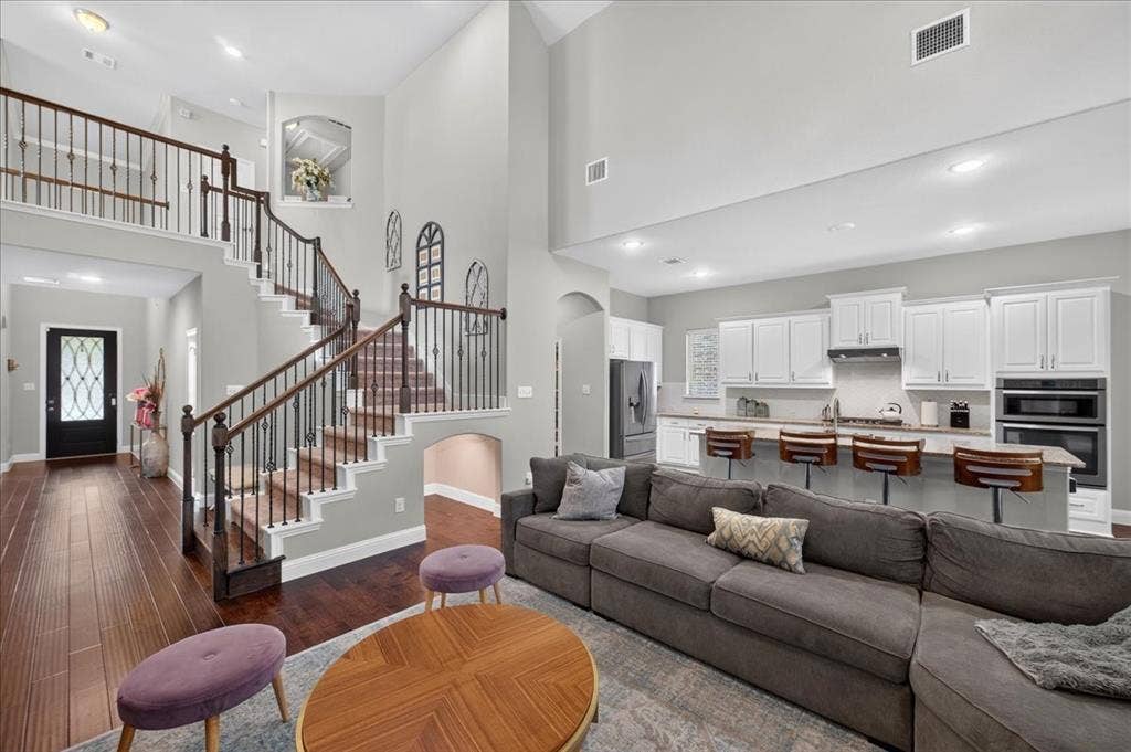 8712 Mccutchins Drive, McKinney, TX 75070 Two-story living area with high ceilings, wood-finish flooring, and an open-concept kitchen featuring white cabinetry and stainless steel appliances