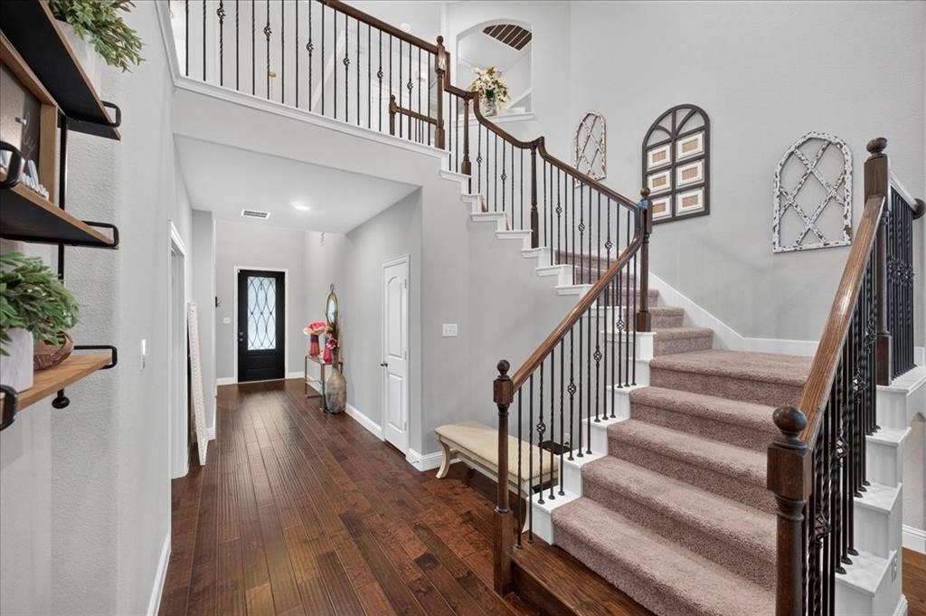8712 Mccutchins Drive, McKinney, TX 75070 Hardwood-finish flooring, two-story foyer, carpeted staircase with wrought iron balusters, wood handrails, and a transom window above the entry