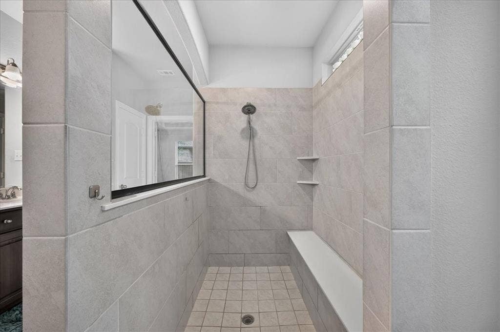 8712 Mccutchins Drive, McKinney, TX 75070 Expansive shower stall featuring light-toned tile, a built-in bench, two recessed shelves, and a large fixed glass panel