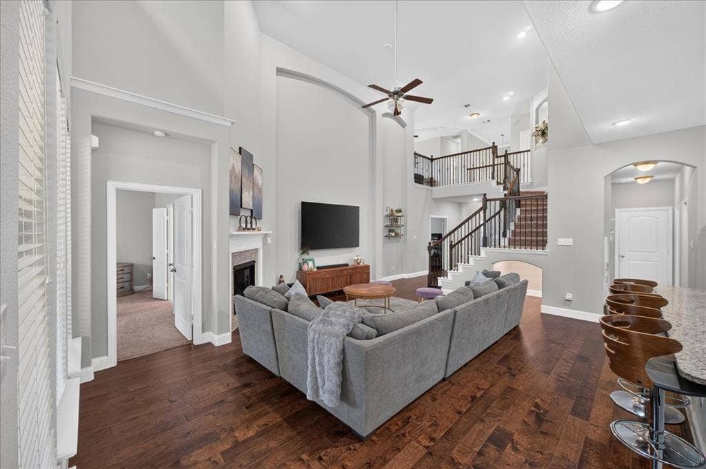 8712 Mccutchins Drive, McKinney, TX 75070 Hardwood-style flooring throughout the main living area, fireplace with mantel, two-story ceiling, and a multi-level staircase with dark wood railings