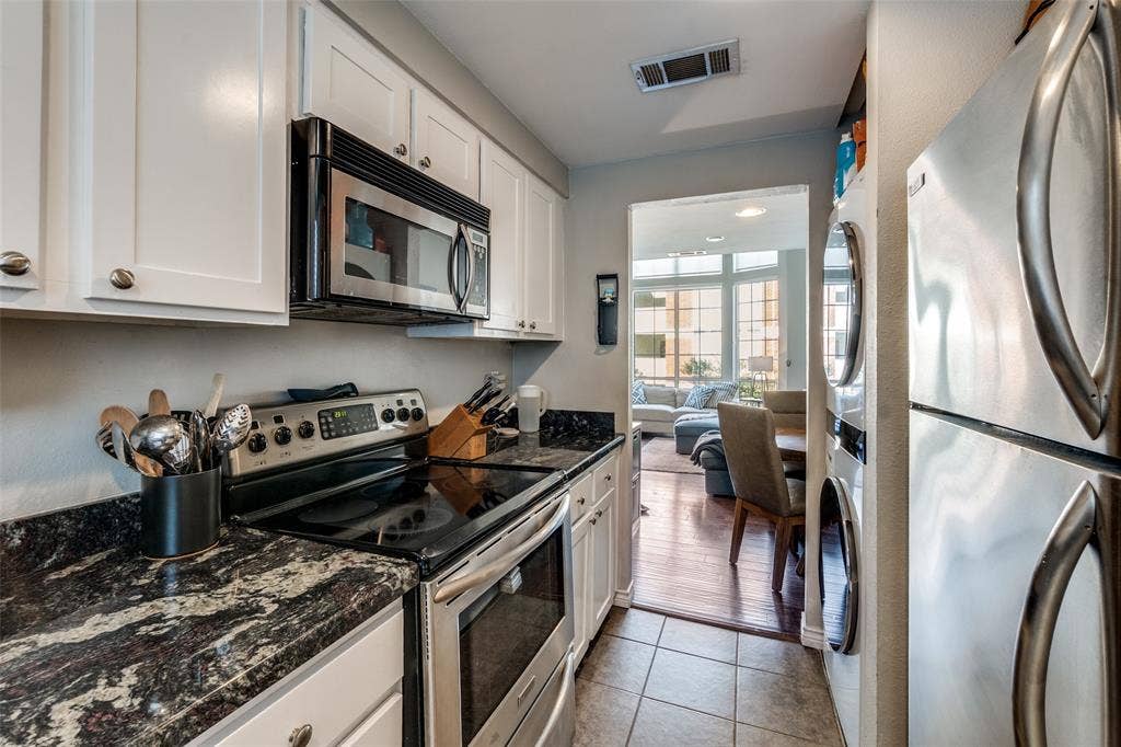 3100 Cole Avenue, #213, Dallas, TX 75204 Kitchen with appliances with stainless steel finishes, white cabinetry, dark stone countertops, and light tile patterned flooring