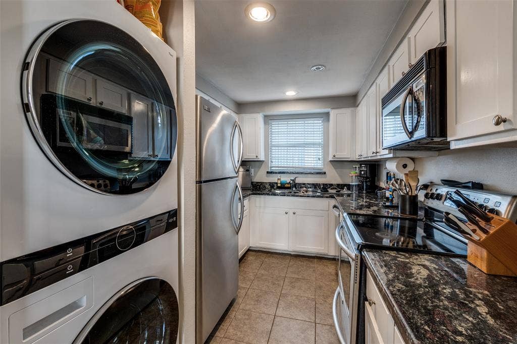 3100 Cole Avenue, #213, Dallas, TX 75204 Kitchen featuring stainless steel appliances, dark stone countertops, white cabinetry, estacked washer and dryer, and light tile patterned flooring