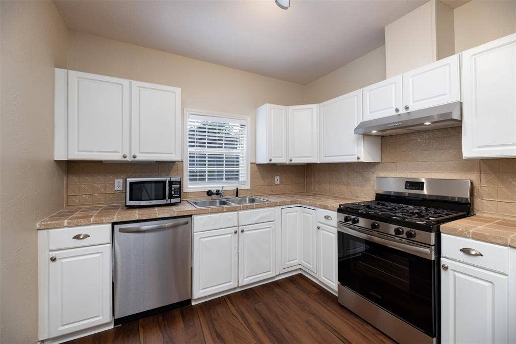 8823 San Benito Way, Dallas, TX 75218 Full kitchen featuring white cabinetry, tile countertops, tile backsplash, stainless steel appliances, and wood-finish flooring